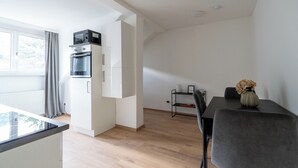 Een moderne keuken met inbouwapparatuur, een eethoek met een tafel en stoelen, en een klein wandrek.