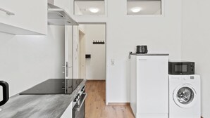 Een kleine keuken met een kookplaat, magnetron en wasmachine, een houten vloer en inbouwverlichting.