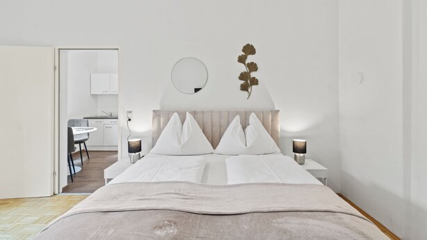 Een moderne hotelkamer met een bed, nachtlampjes, een spiegel en een klein tafeltje.