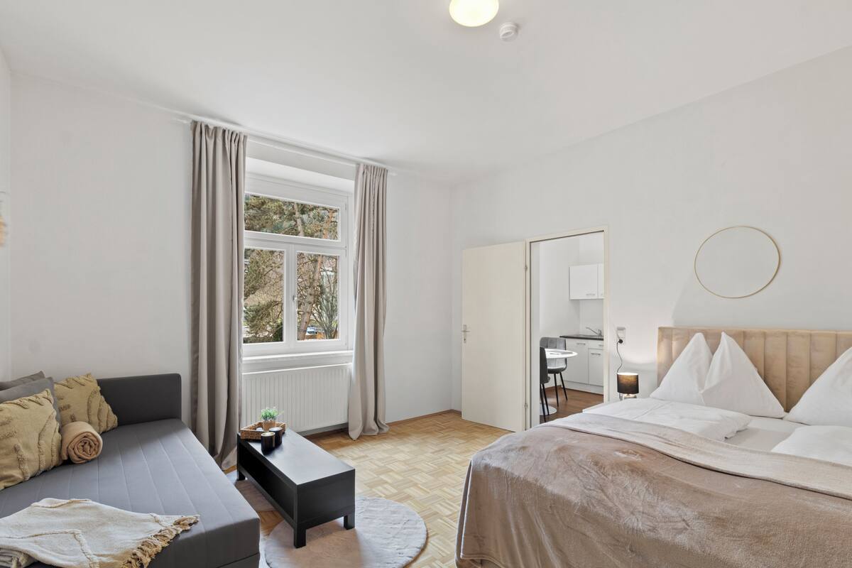 A hotel room with a bed, a sofa, a small table, a desk, and a window with curtains.