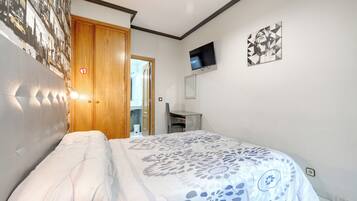Un dormitorio con cama, una puerta de madera, un escritorio, una silla, un televisor y una pared con un mural de paisaje urbano.