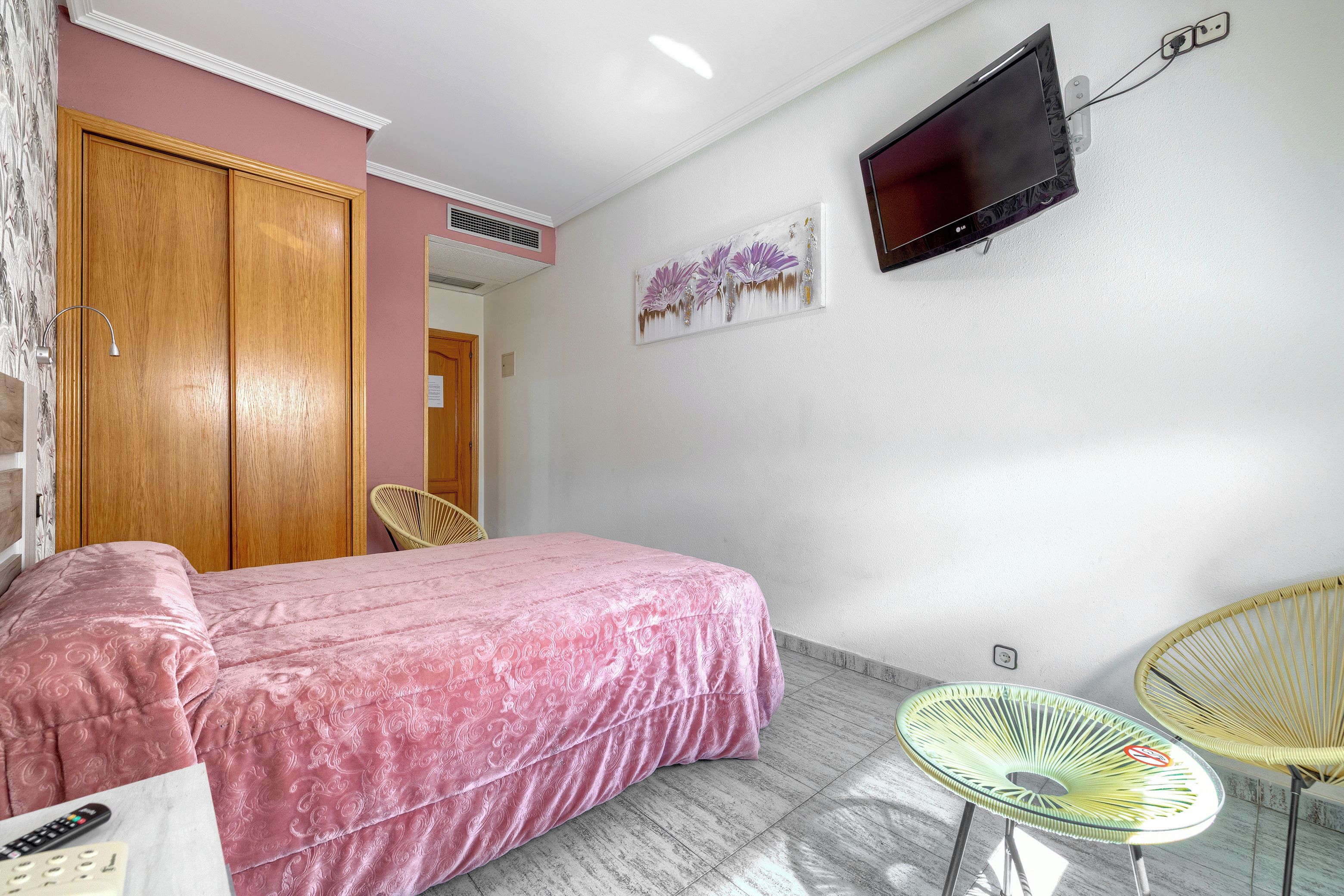 Un dormitorio con cama, televisor, armario y dos sillas.