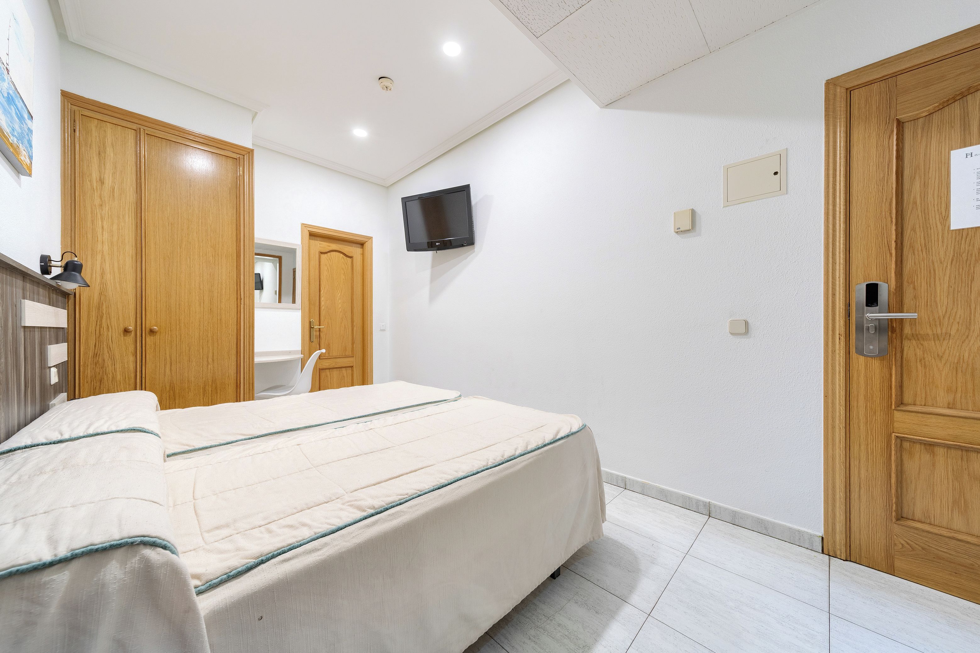 Ein Hotelzimmer mit Bett, Holzschrank, Wandfernseher und einer Tür mit Schloss.