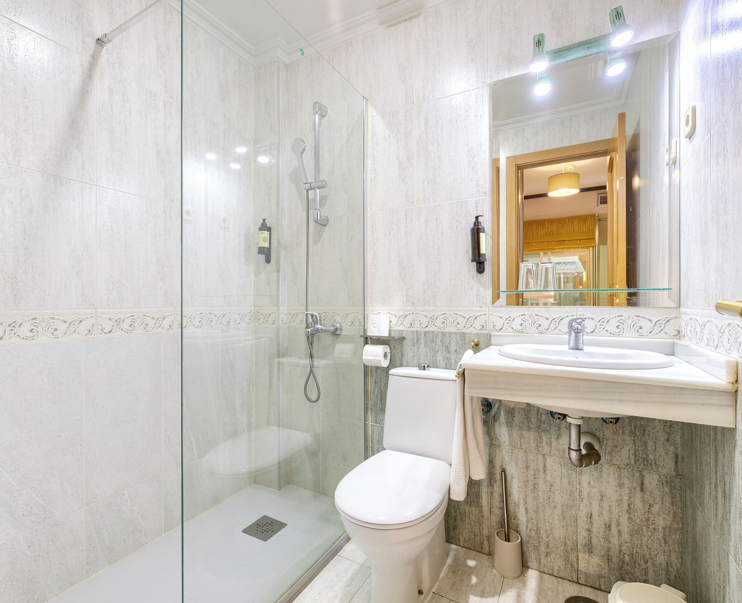 Un baño con ducha separada por vidrio, inodoro y lavamanos con espejo.