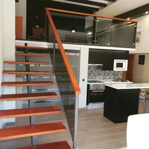 A modern kitchen with a microwave, oven, and a glass staircase leading to an upper level.