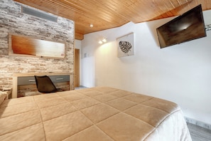 A bedroom with a bed, a desk, a chair, a TV, and a wall-mounted heater.