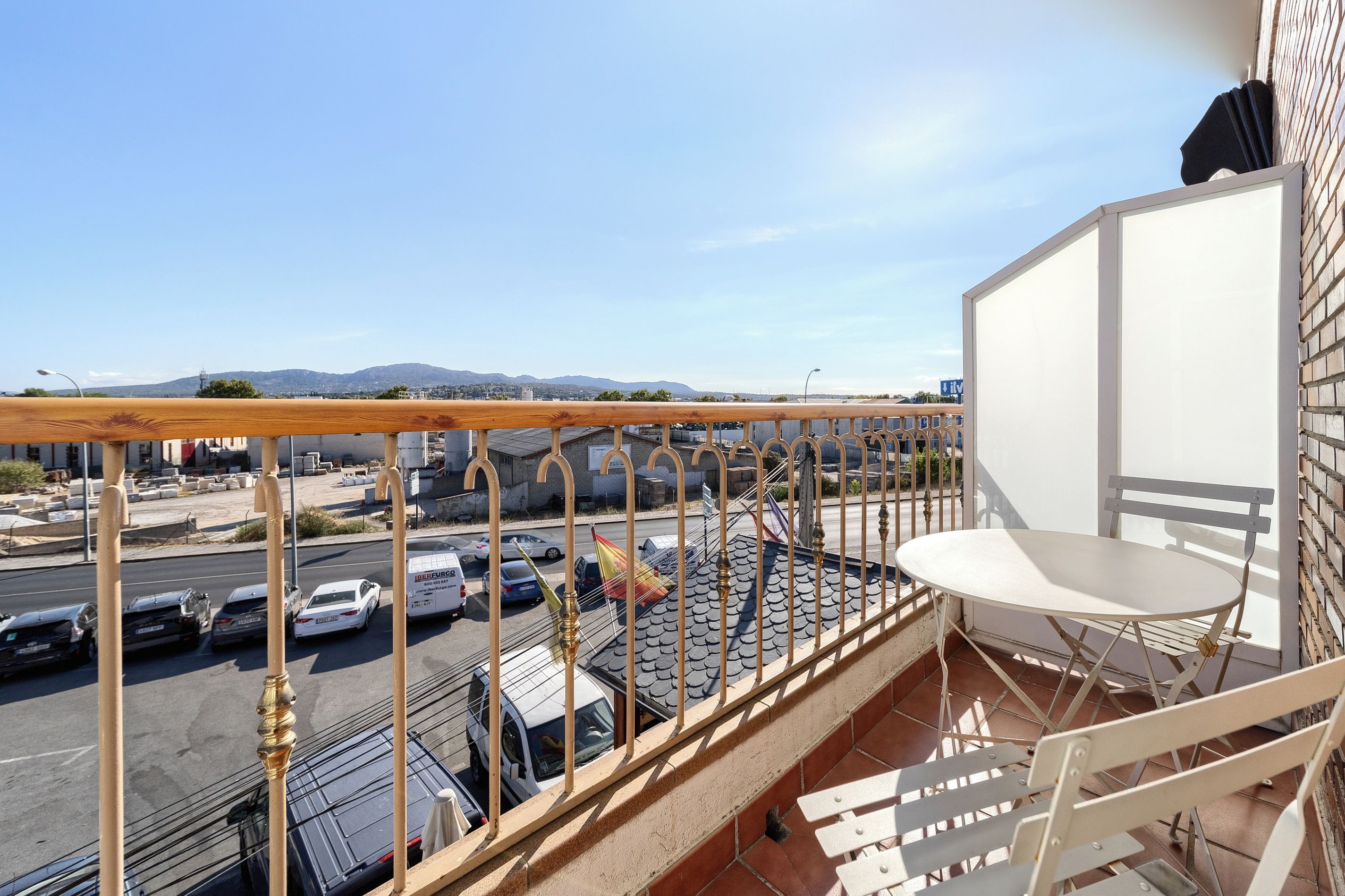 A balcony with a view of a parking lot and mountains in the distance.