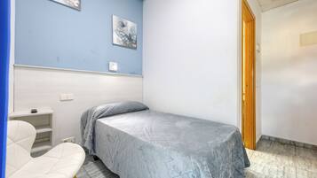 Une petite chambre avec un lit simple, un mur bleu, une chaise blanche et une porte en bois.
