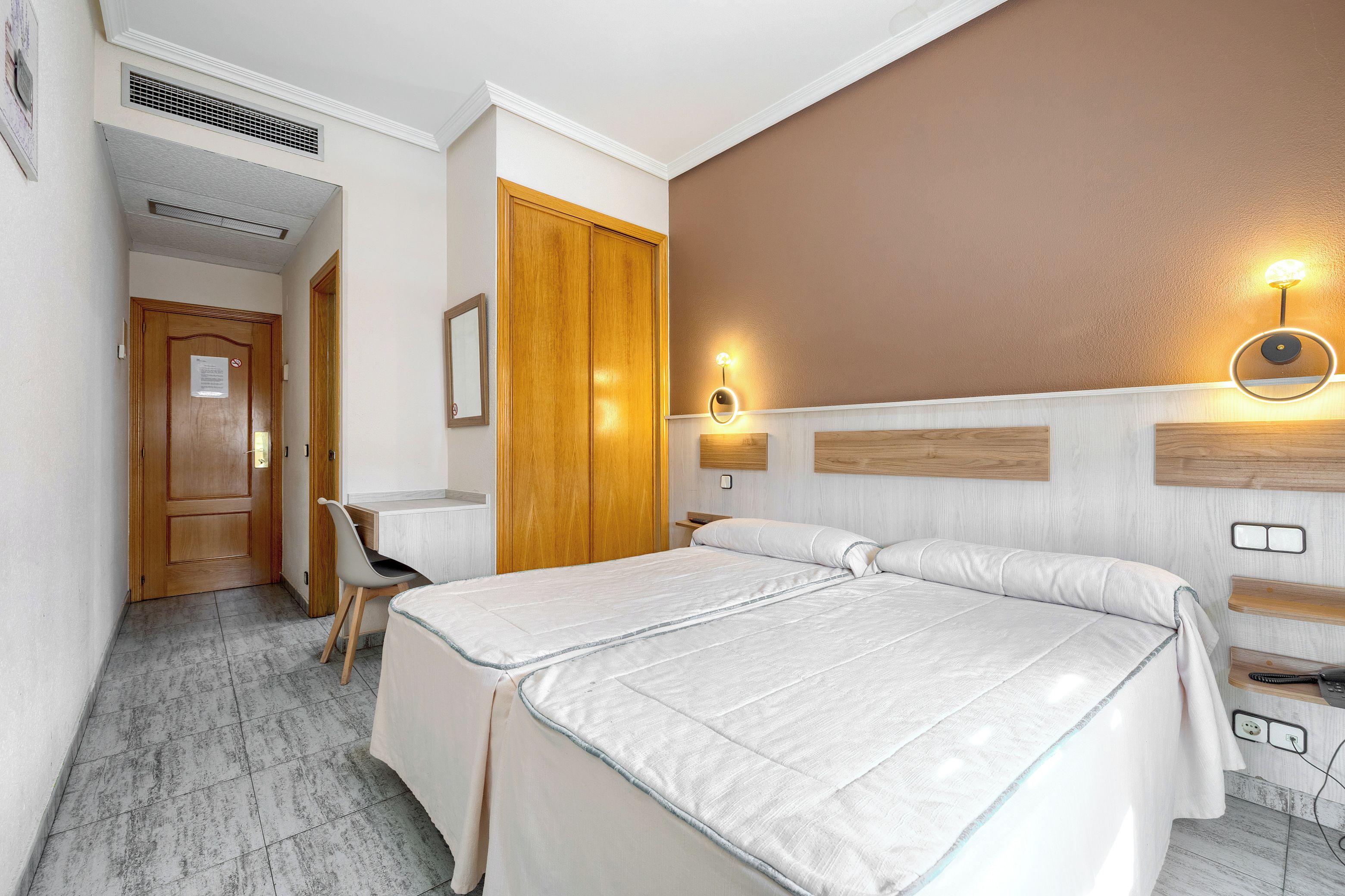 A hotel room with two beds, a desk, a chair, a wardrobe, and a bathroom.