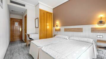 A hotel room with two beds, a desk, a chair, a wardrobe, and a bathroom.