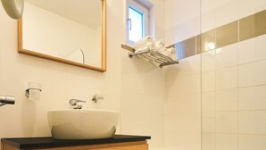 A modern bathroom with a wooden vanity, a large mirror, a white sink, and a glass shower enclosure. - PRIVILEGE 2-Bedroom Cottages (Parentis-en-Born)