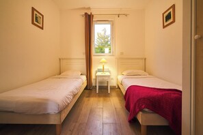 Eine kleine, einfache Unterkunft mit zwei Betten, einem Nachttisch mit Lampe und einem Fenster mit Vorhängen.