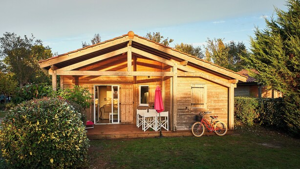 A wooden house with a porch, a bicycle, and a small table with chairs. - PRIVILEGE 2-Bedroom Cottages (Parentis-en-Born)