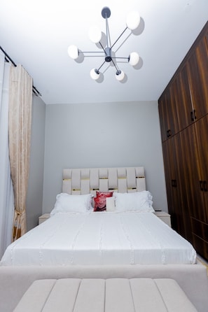 Un dormitorio con cama, cabecera, armario y lámpara en el techo.