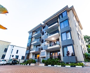 A multi-story residential building with balconies, a driveway, and a parked vehicle. - Imaani Homes  (Kampala)
