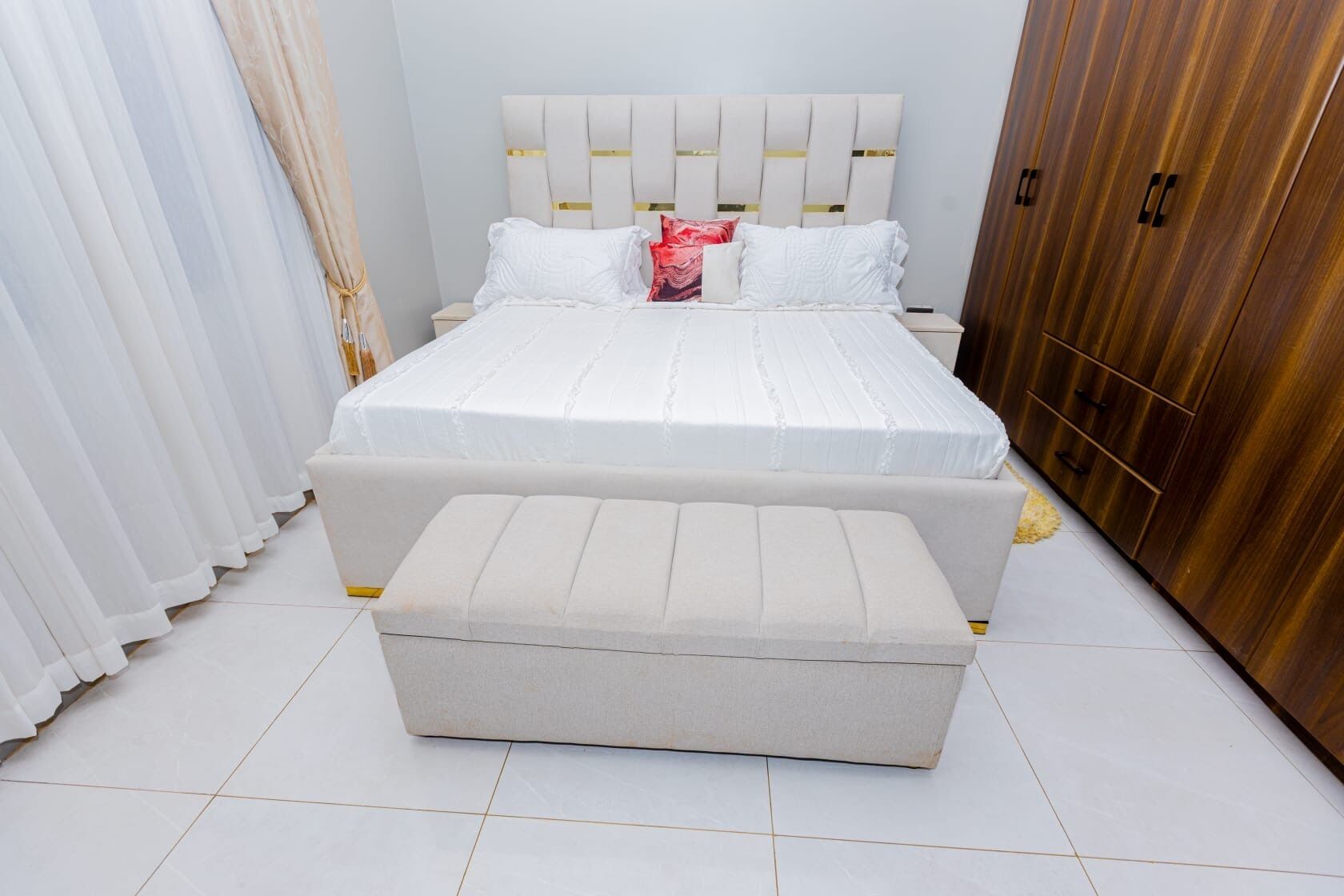 A bedroom with a bed, a bench, a wardrobe, and curtains.