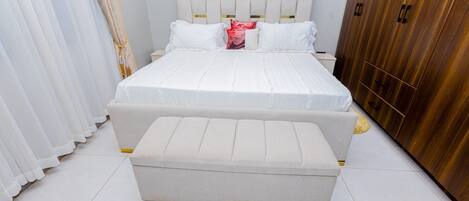 A bedroom with a bed, a bench, a wardrobe, and curtains.
