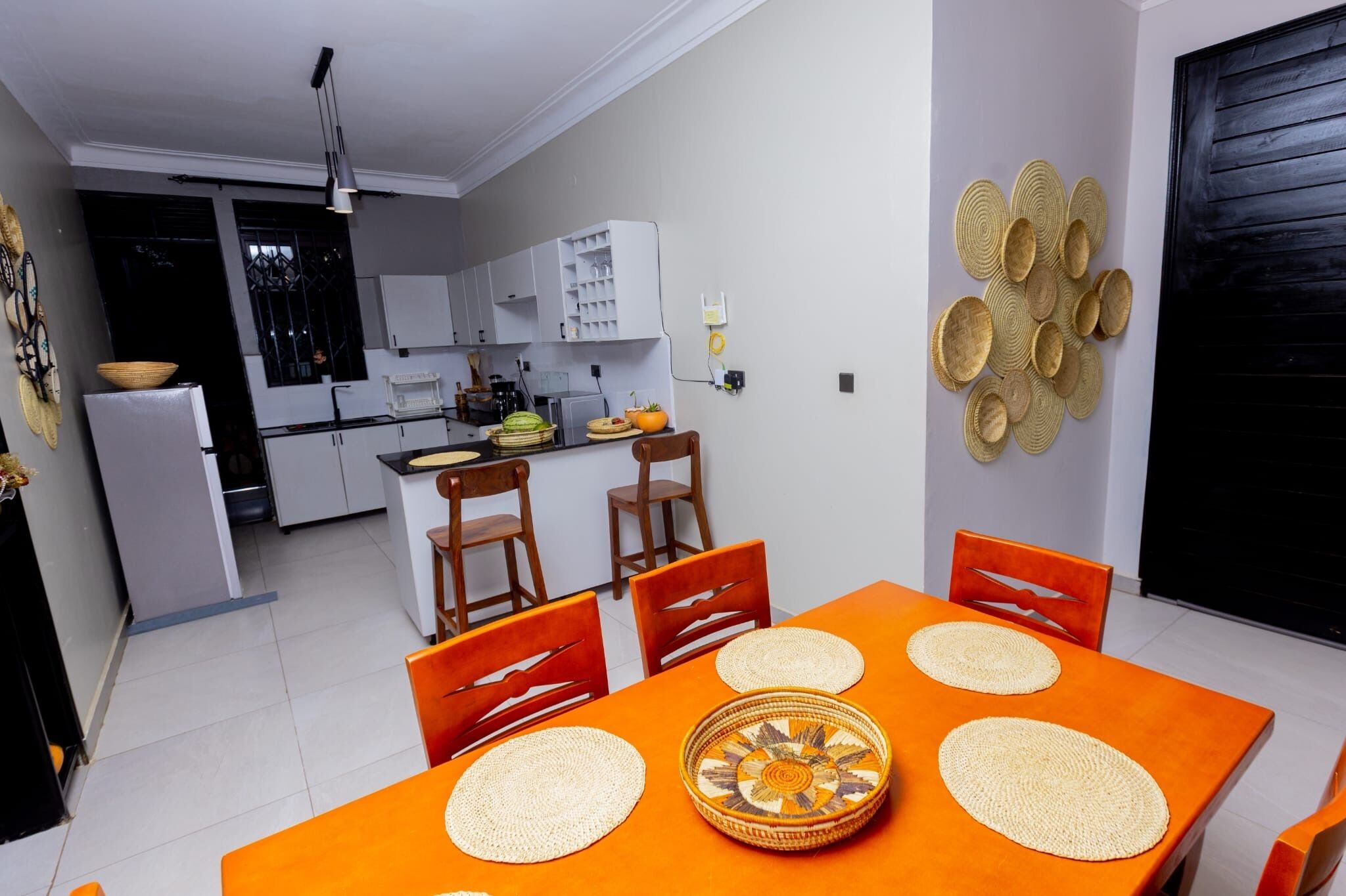 A dining area with a table set for four, a kitchen in the background, and a decorative wall piece.