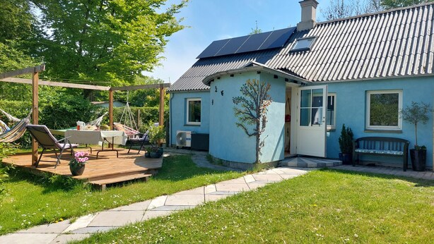 Ein Haus mit Garten, einer Holzterrasse, einer Hängematte, einem Tisch und einer Bank.
