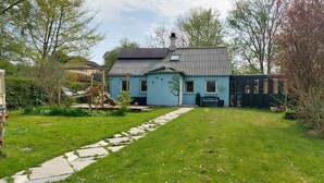 Ein Haus mit blauer Fassade, einem Steinweg, der zur Haustür führt, und einem kleinen Garten mit einer Hängematte und einer Bank.