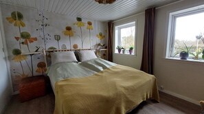 A bedroom with a bed, a window with curtains, and a wall with floral decorations. - En perle på Møn nær sandstrand. God til 2 familier. kæledyrsvenlig (Askeby)