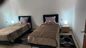 A room with two single beds, each with a headboard and a bedside table with a lamp. The room has a tiled floor and a rug. - COTE (Djerba - Houmt Souk)