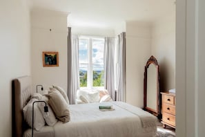 A bedroom with a bed, a dresser, a mirror, and a window with curtains.
