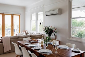 A dining area with a wooden table set for a meal, a sofa in the background, and large windows with a view.
