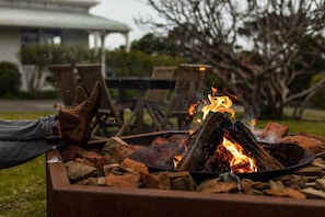 Ein Lagerfeuer mit Holzscheiten und einem Glas Rotwein, umgeben von Gartenmöbeln.