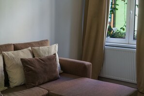 Ruskea sohva, jossa on useita koristetyynyjä, ikkuna, jossa on verhot, ja näkymä vehreään maisemaan.