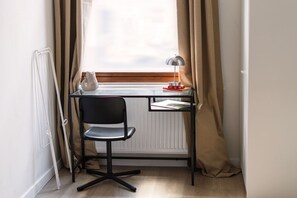 Ett arbetsområde med ett skrivbord, en stol, en lampa, ett element och ett fönster med gardiner.