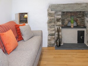 Ein Wohnzimmer mit Kamin aus Stein, einer Couch mit orangenen Kissen und einer Vase mit Blumen.