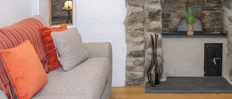 A living room with a stone fireplace, a sofa with orange cushions, and a vase with flowers.