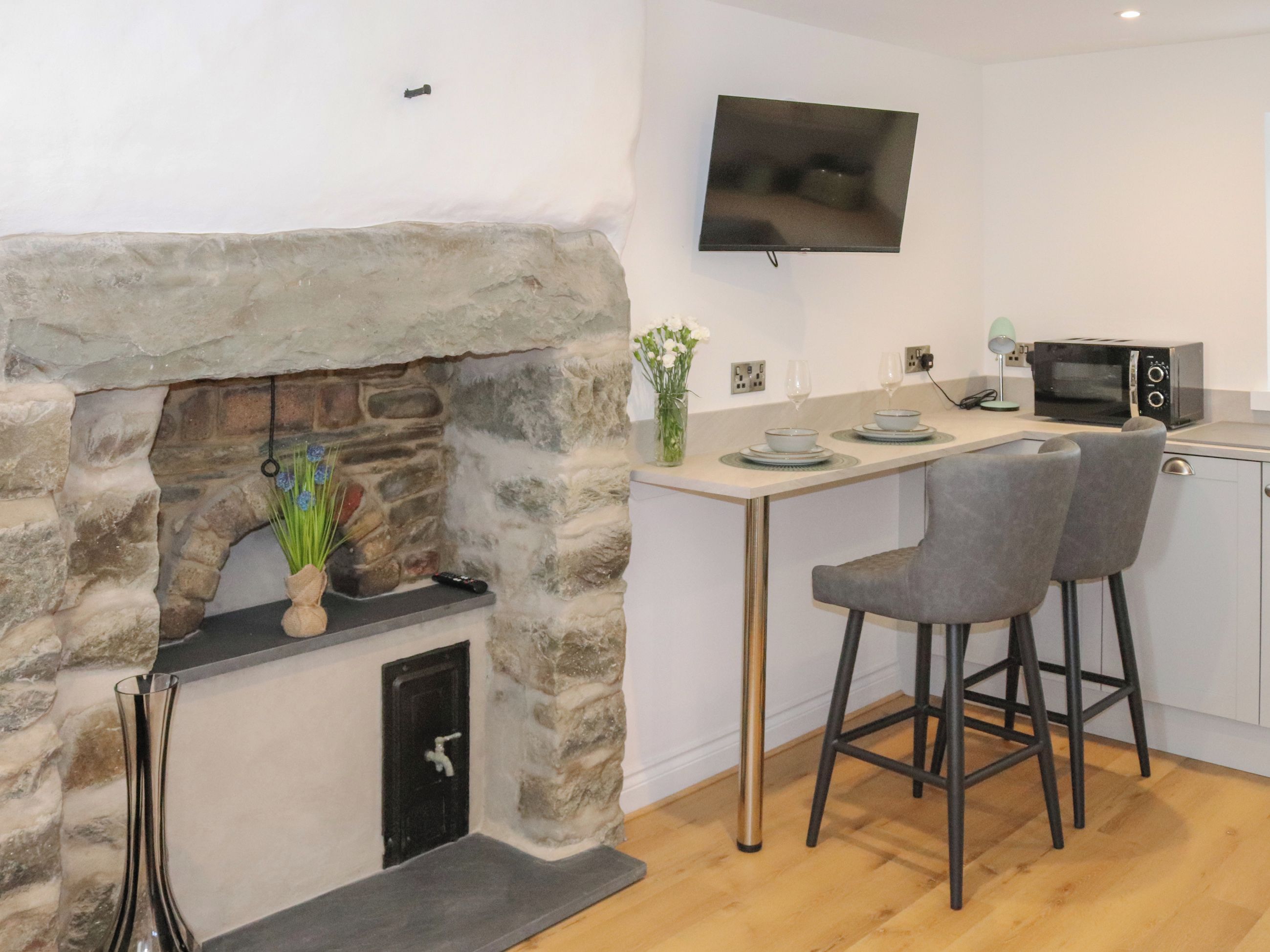 Una cocina con chimenea de piedra, un televisor de pantalla plana, un microondas y dos taburetes de bar.