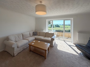 Ein Wohnzimmer mit einem beigefarbenen Sofa, einem Holztisch und Blick auf einen Garten durch ein großes Fenster.