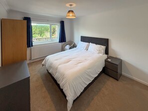Ein Schlafzimmer mit Bett, Nachttischen, einem Fenster mit Vorhängen, einer Heizung und einer Deckenleuchte.