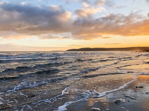 A beach with waves, a sunset, and a distant landmass. - 3 bedroom accommodation in Benllech (Benllech)