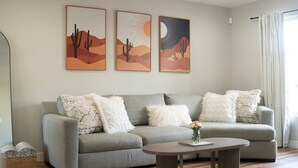 A living room with a grey sofa, white fluffy cushions, a round coffee table, and three desert-themed wall art pieces. - 4-bdrm home with 2 Master Suites & Heated Pool minutes from Old Town Scottsdale (Scottsdale)