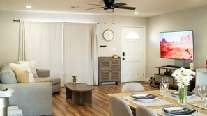 Una sala de estar con un sofá, una mesa de centro, una mesa de comedor preparada para dos personas y un televisor montado en la pared.