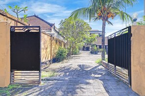 A paved pathway leading to a gated entrance, flanked by buildings with tiled roofs and a palm tree. - Stylish Double Suite Escape W/ Free Wifi (Kedonganan)