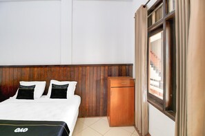A hotel room with a bed, a wooden wardrobe, and a window with curtains.