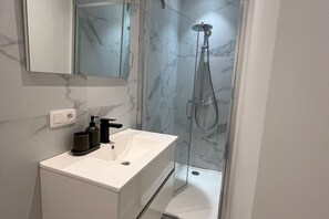A modern bathroom with a white sink, a mirror, and a glass-enclosed shower. - Central 1BR Apartment for 4 | Prime Location (Ghent)