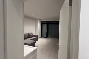 A modern living room with a grey sofa, a small table, and a sliding glass door leading to a balcony. - Central 1BR Apartment for 4 | Prime Location (Ghent)