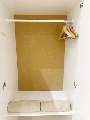 Un armario blanco con un perchero marrón, perchas de madera y una toalla beige enrollada.