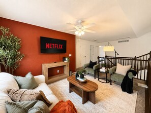 A living room with a TV mounted on a red wall, a wooden coffee table, and a staircase leading to another level. - 3200 sqft • 5BRD • 9 beds • sleeps 16• Games (Denver)