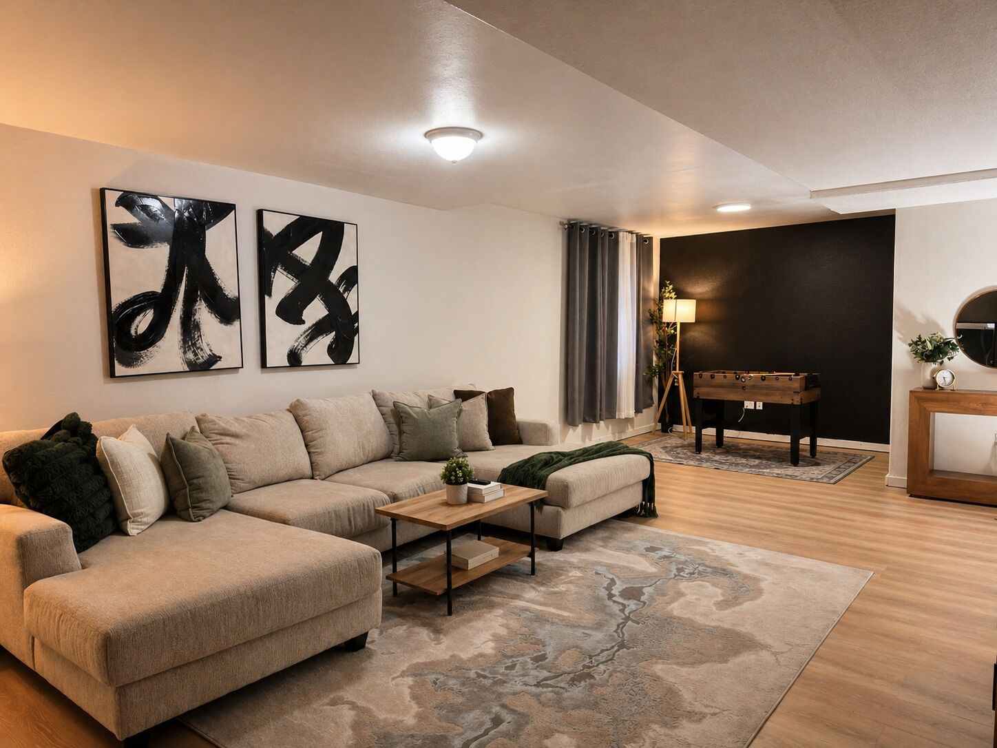 Un salon moderne avec un canapé d’angle, une table basse, des œuvres d’art abstraites, un baby-foot et un mur d’accent de couleur foncée.