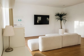 A modern living room with a flat-screen TV, a potted plant, and a white sofa. - New 2BR Apartment near Dreamland Beach (Kuta)
