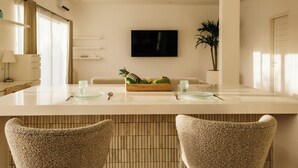 A modern kitchen with a white countertop, a fruit basket, two chairs, and a potted plant.
