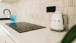 A kitchen with a white countertop, a black induction cooktop, a white coffee maker, and a blue water dispenser.