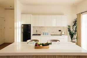 Una cocina moderna con armarios blancos, una isla central con fruta y una planta en maceta.